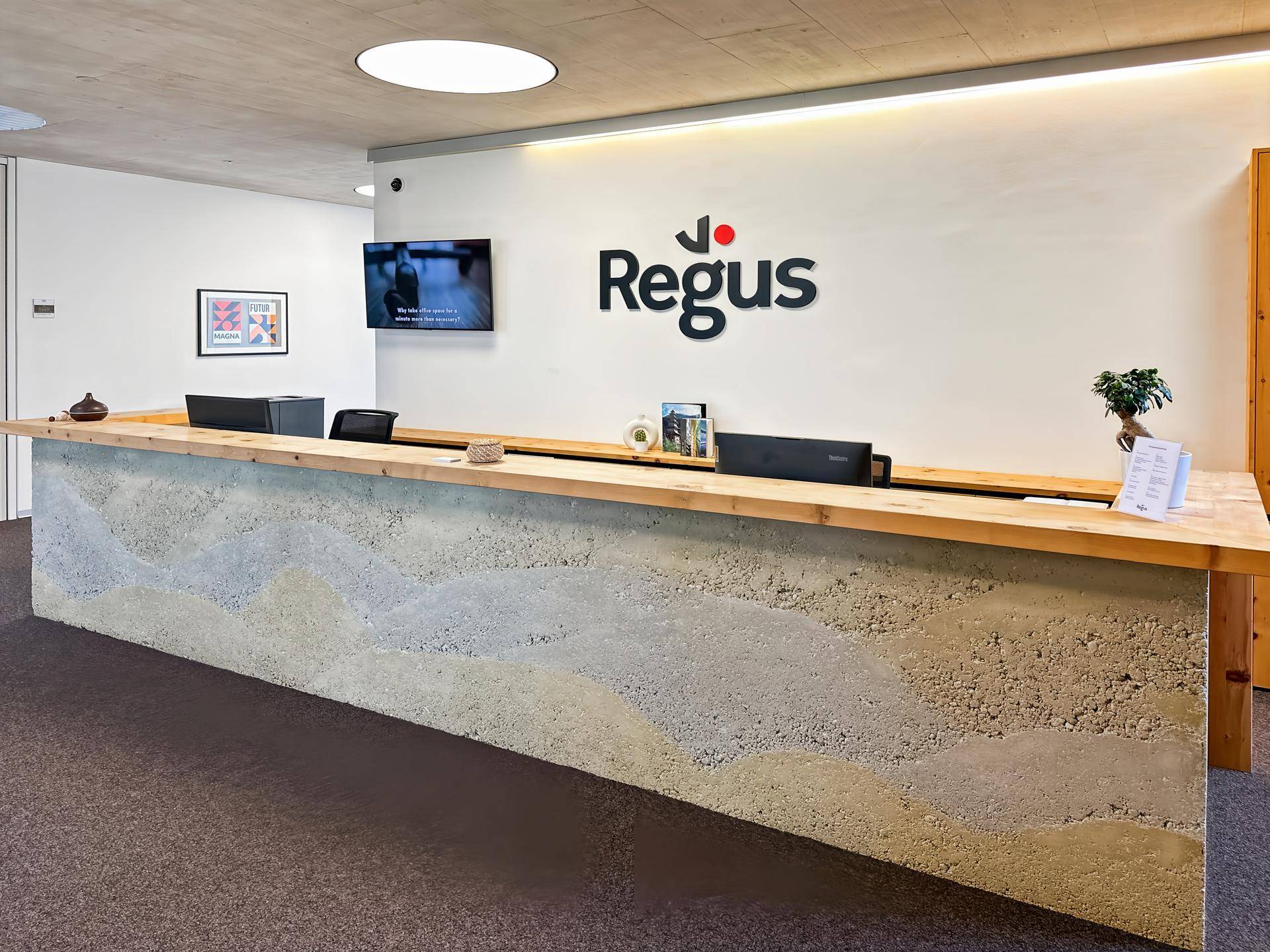 Empfangsbereich mit einer markanten Rezeptionstheke aus Holz und strukturiertem Beton sowie dem Regus-Logo an der Wand.