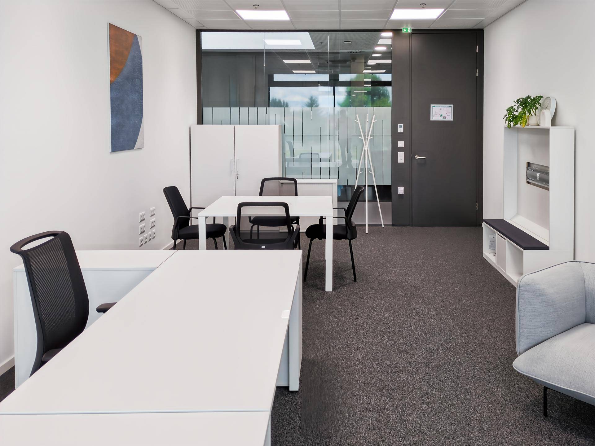 Helles Büro mit Schreibtischen, Stühlen und einer Garderobe, ideal für konzentriertes Arbeiten.