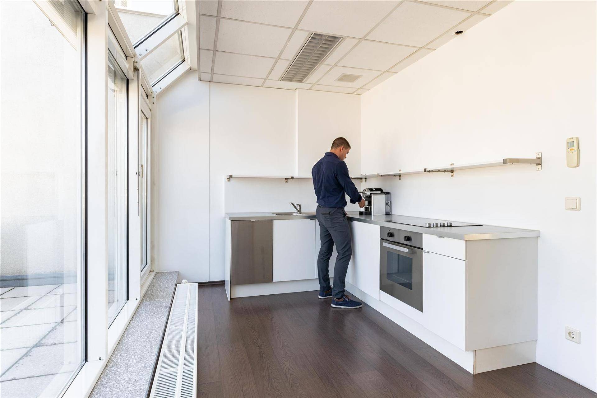 Kleine Büroküche mit dunklem Holzboden, weißen Schränken, modernen Geräten und Zugang zu einem Außenbereich.