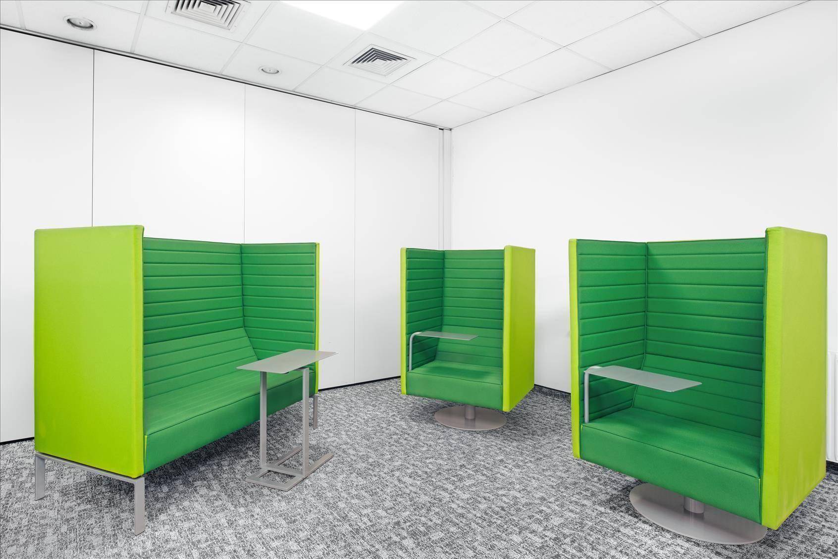 Helle Lounge-Zone mit drei modernen, grünen Sitzkabinen und einem gemusterten Teppichboden in einem Büro.