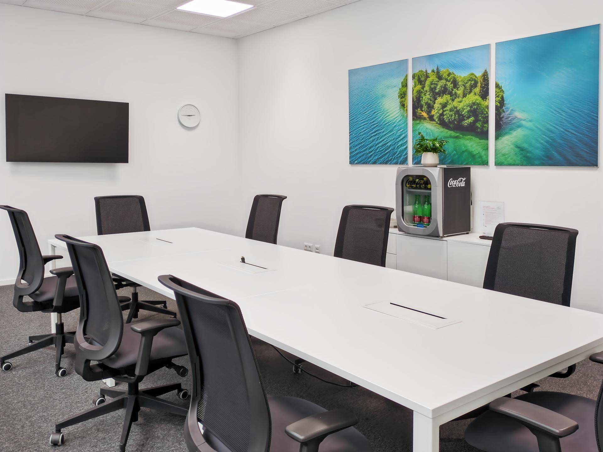 Heller Konferenzraum mit großem weißen Tisch, Bürostühlen und einem Wandbild mit Naturmotiv.