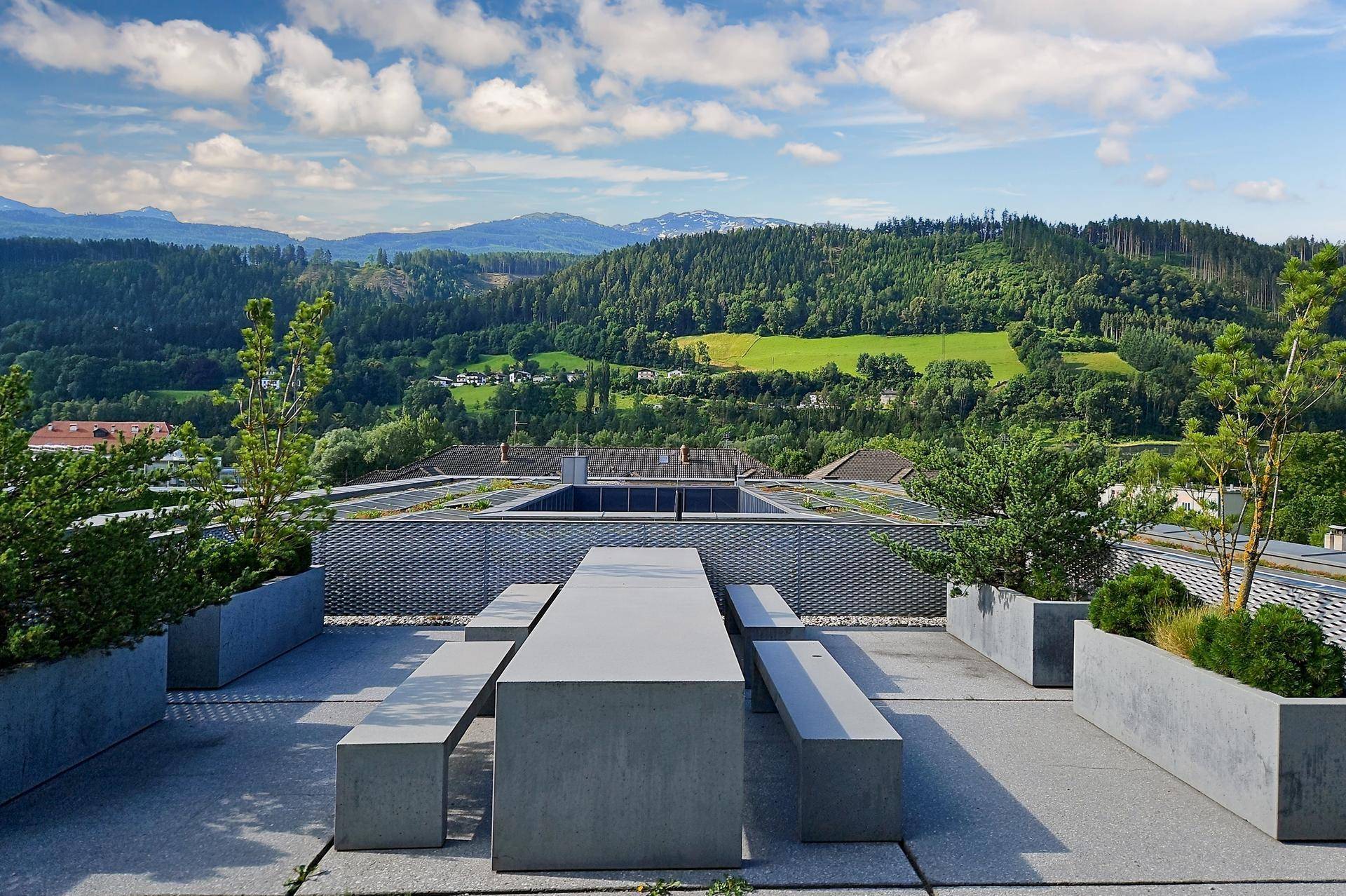 Dachterrasse mit moderner Sitzgruppe und weitem Panoramablick auf die umliegende Berglandschaft und grüne Hügel.