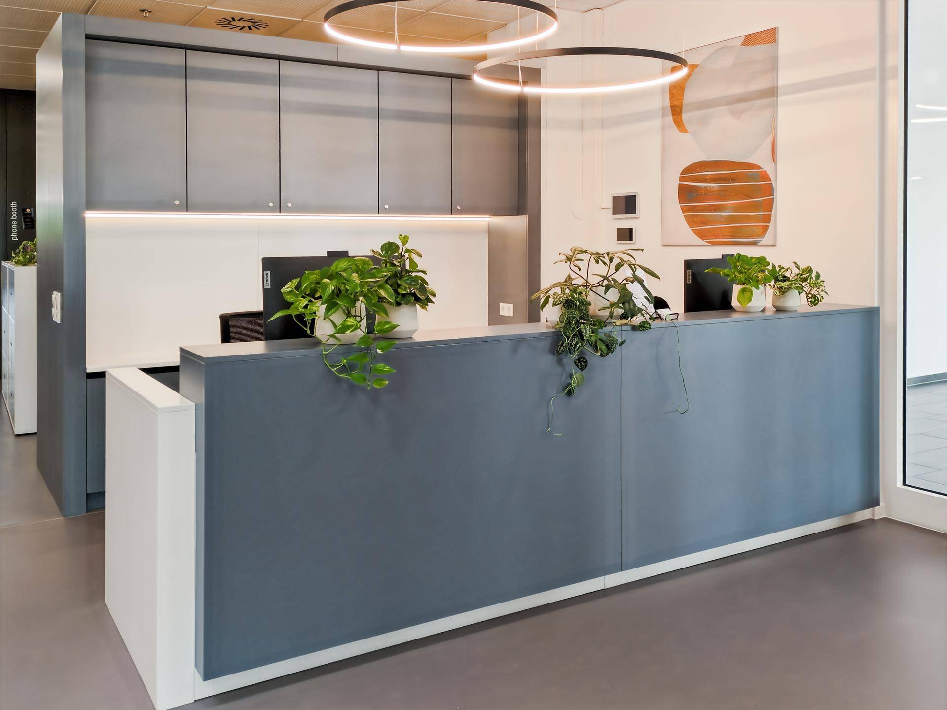 Moderner Empfangstresen in Grau mit Pflanzen und abstrakten Kunstwerken an der Wand.