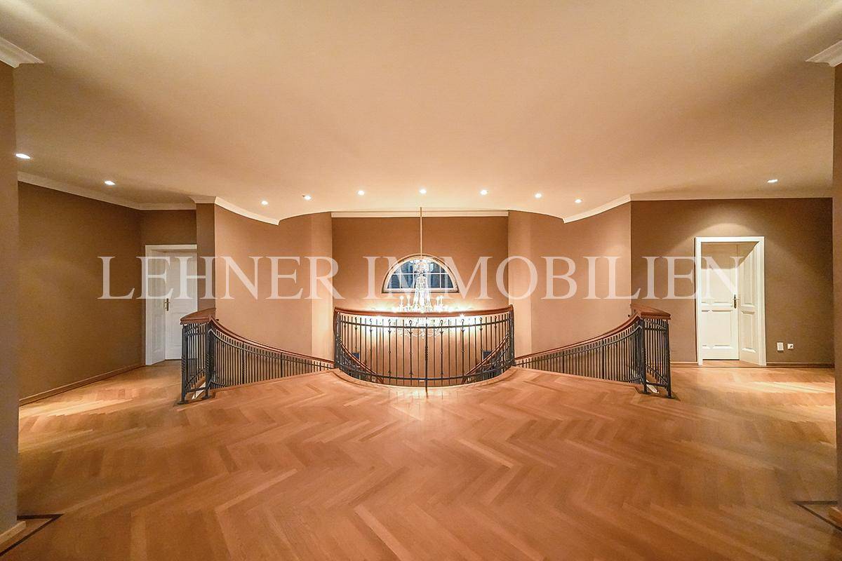 Eleganter Treppenabsatz mit Fischgrätparkett und geschwungenem Geländer, das den Raum öffnet.