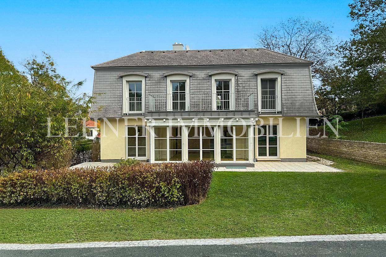 Rückansicht der Villa mit großer Terrasse, Wintergarten und gepflegtem Garten.
