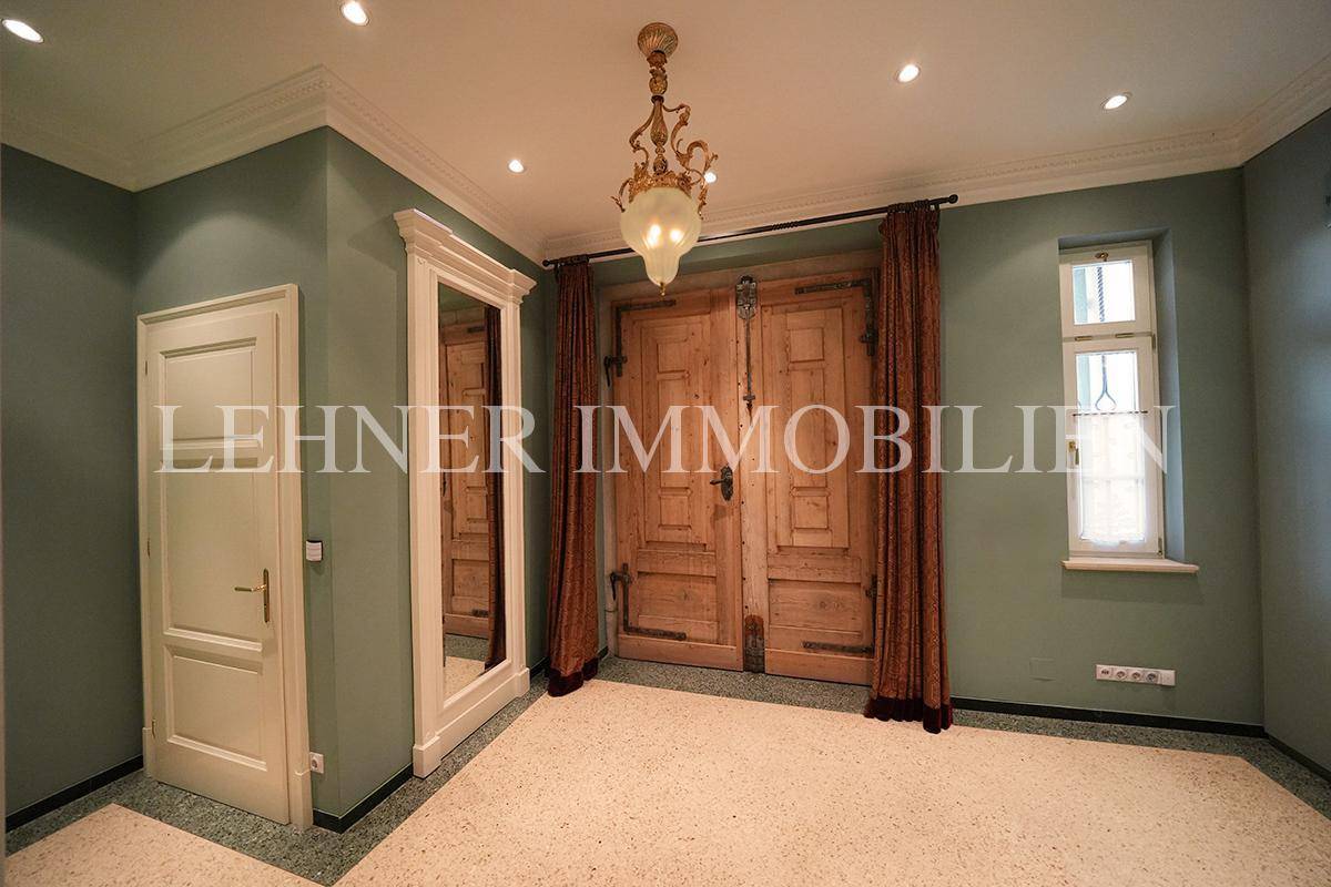 Eingangsbereich mit Terrazzoboden, hohen Holztüren und indirekter Beleuchtung.