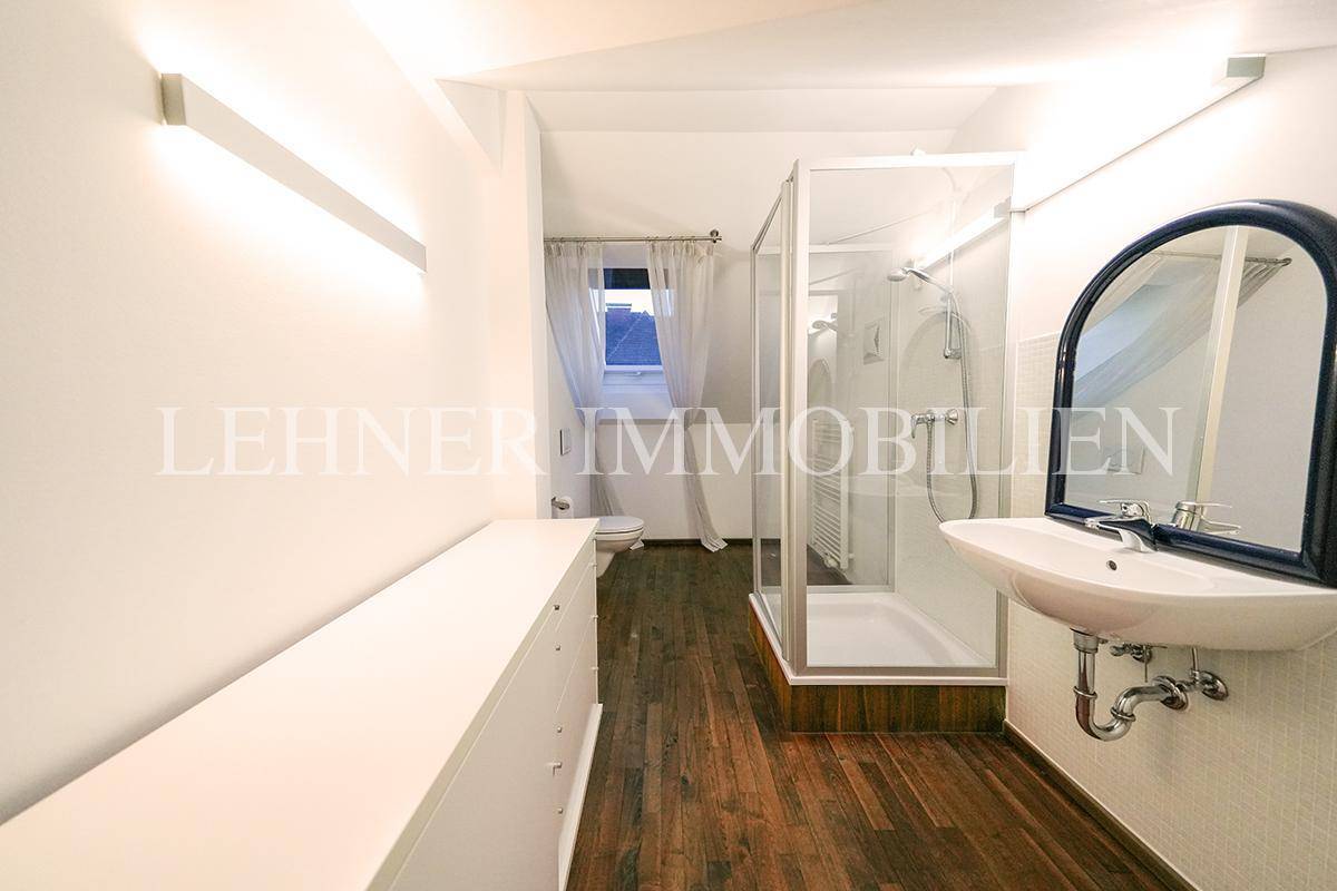 Modernes Badezimmer im Dachgeschoss mit Duschkabine, Waschbecken und Holzboden.