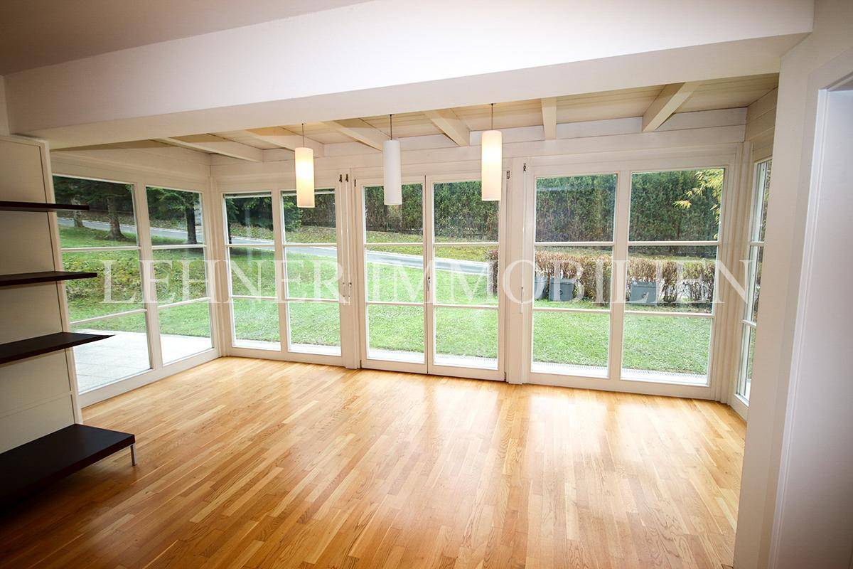 Lichtdurchflutetes Wohnzimmer mit Holzboden, großen Fenstern und Blick in den Garten.