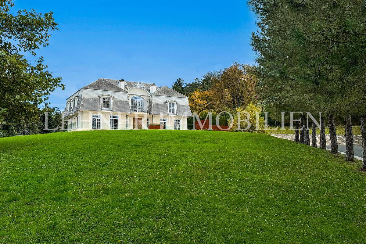 Majestätische Villa auf einem Hügel mit weitläufiger Rasenfläche und altem Baumbestand im Hintergrund.