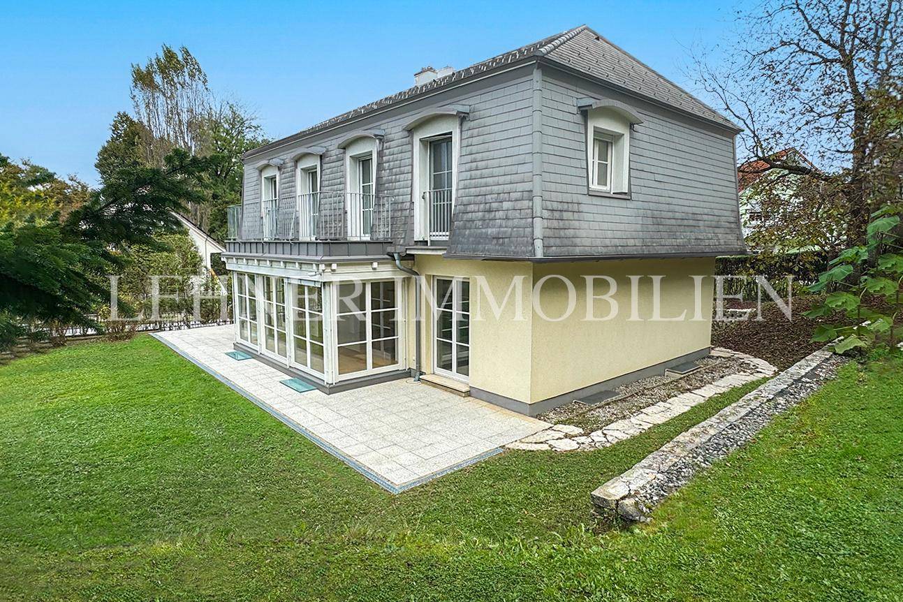 Seitenansicht der Villa mit großer Terrasse, Wintergarten und angrenzendem Gartenbereich.