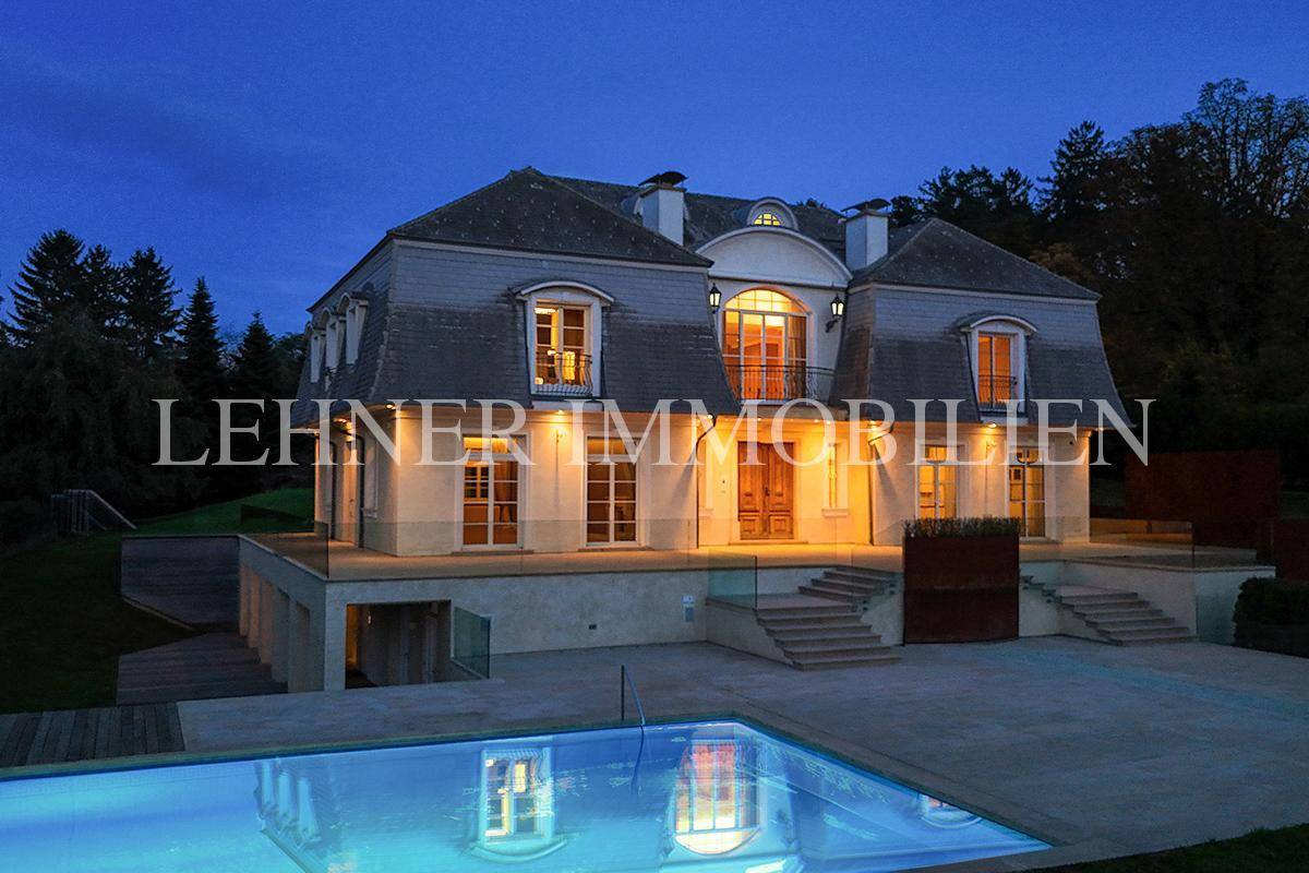 Beleuchteter Swimmingpool und die elegante Villa in der Dämmerung, die eine stimmungsvolle Atmosphäre schafft.