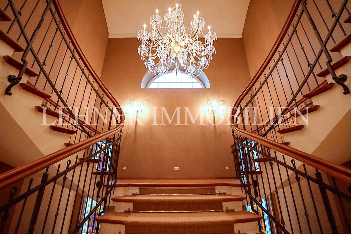 Detailansicht des Treppenhauses mit Kronleuchter, Bogenfenster und Wandleuchten.
