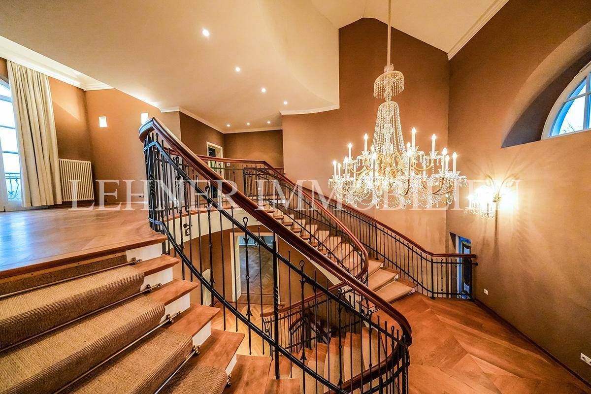 Eindrucksvolles Treppenhaus mit geschwungener Doppeltreppe, Parkettboden und elegantem Kronleuchter.
