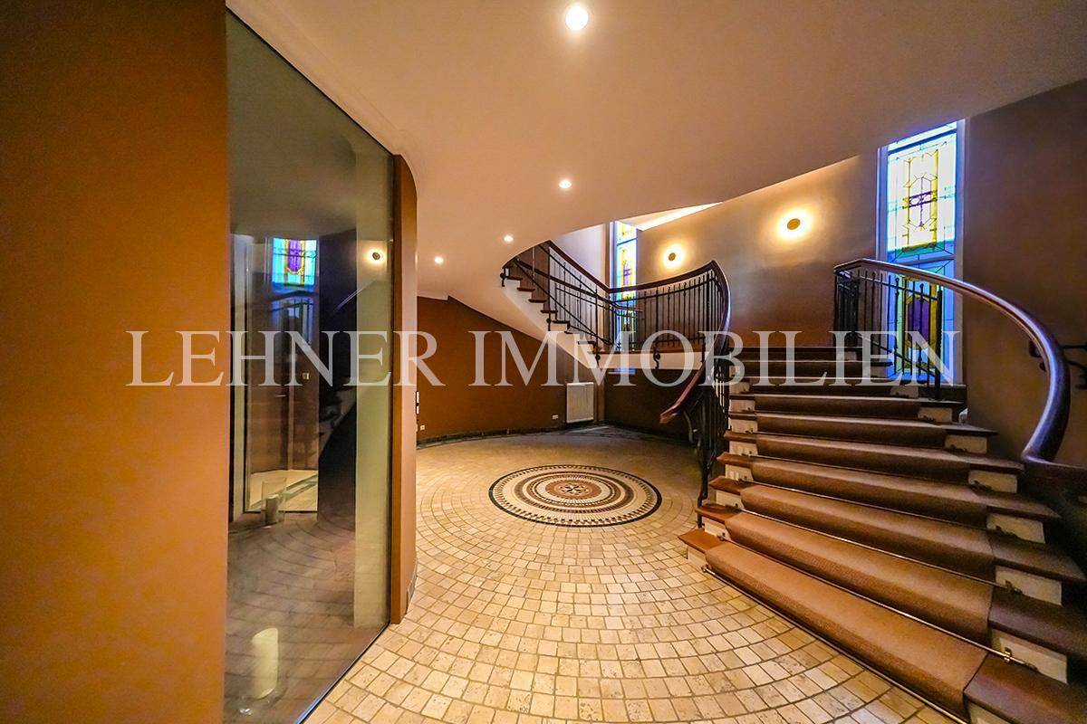 Eindrucksvoller Eingangsbereich mit Mosaikboden, geschwungener Treppe und Buntglasfenstern.