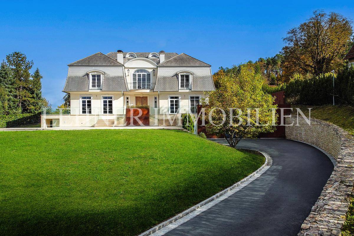 Elegante Villa mit geschwungener Auffahrt, umgeben von gepflegtem Rasen und hohen Hecken.