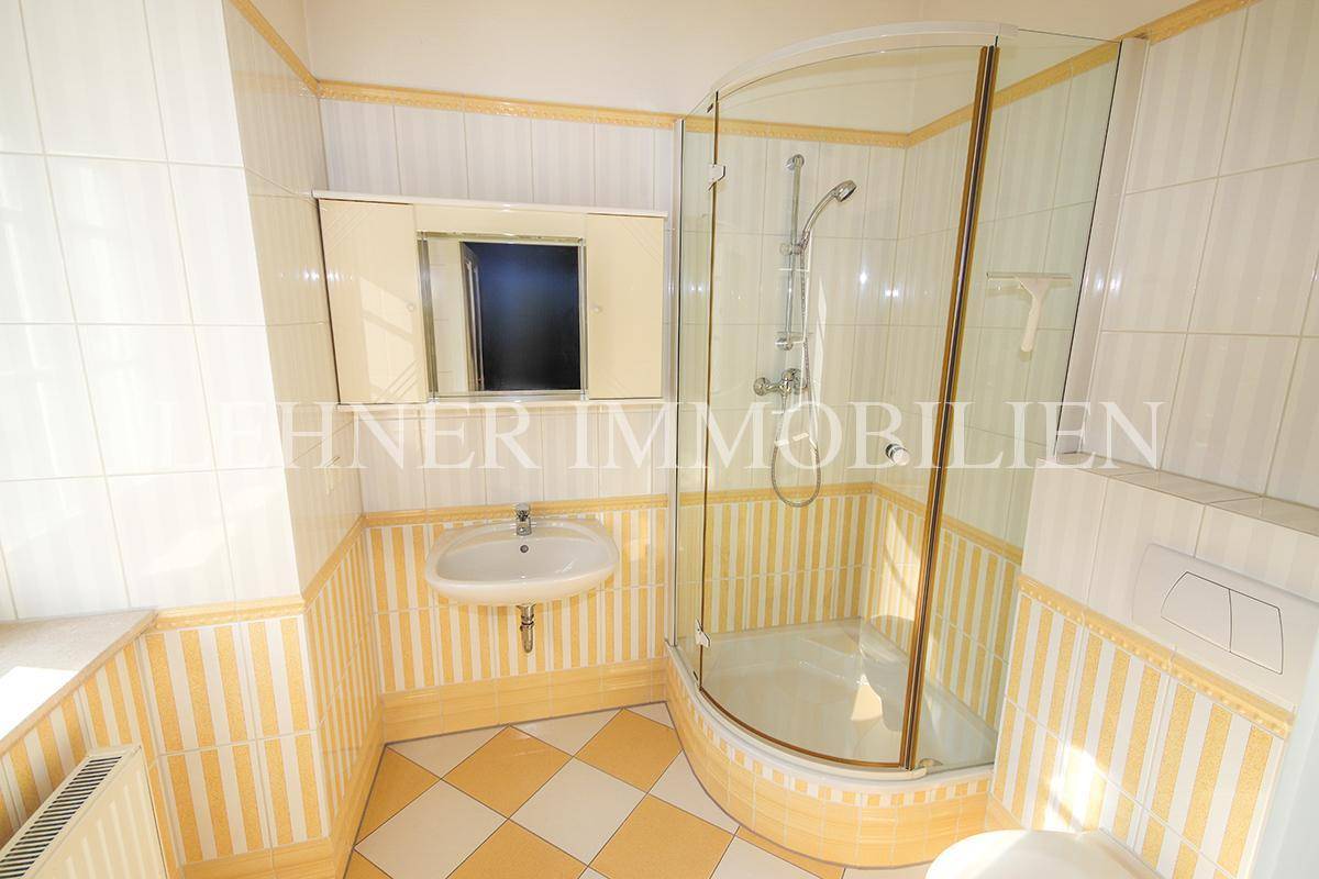 Klassisches Badezimmer mit Duschkabine, Waschbecken und gelb-weiß karierten Fliesen.