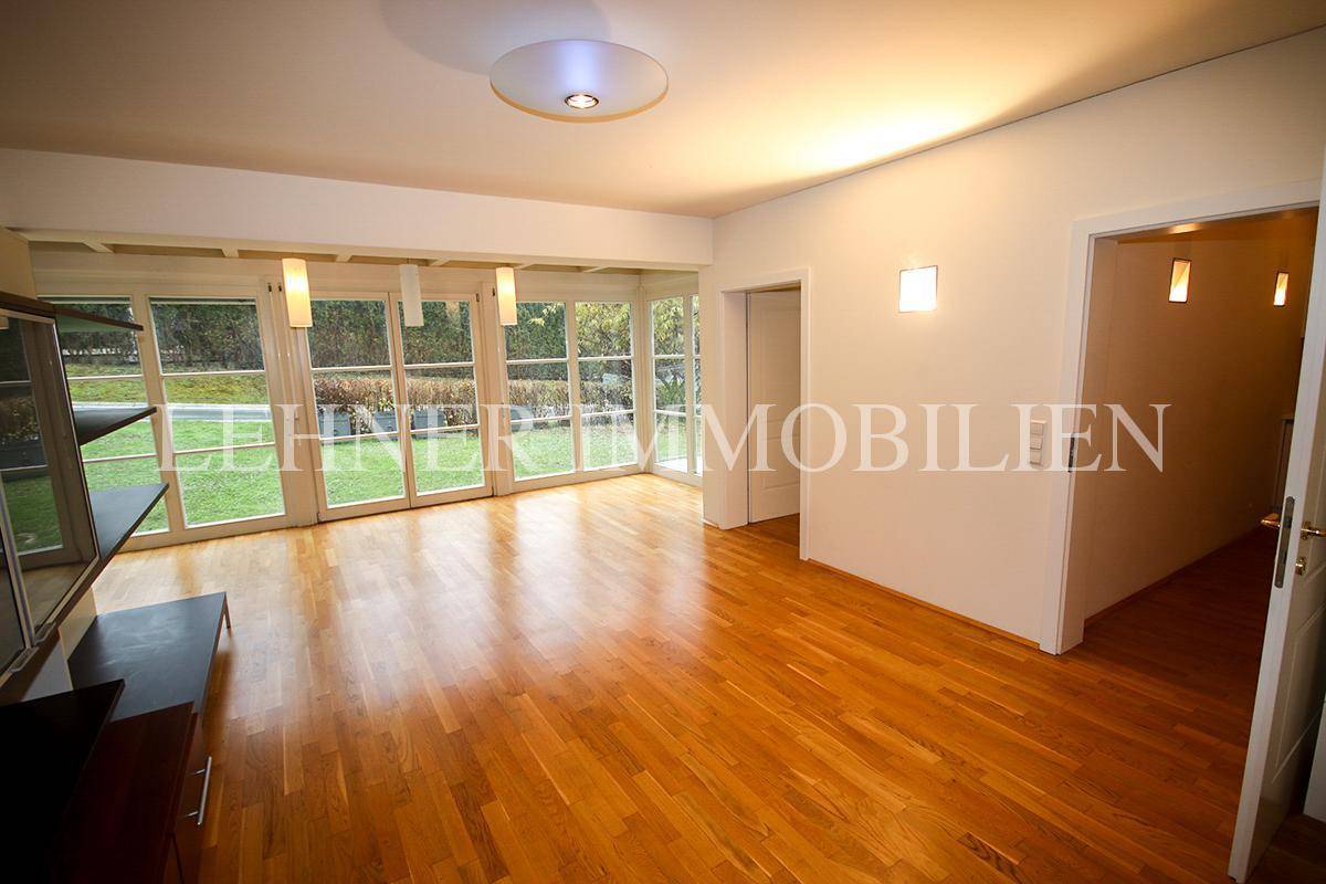 Geräumiges Wohnzimmer mit Holzboden, großen Fenstern und Blick in den Garten.