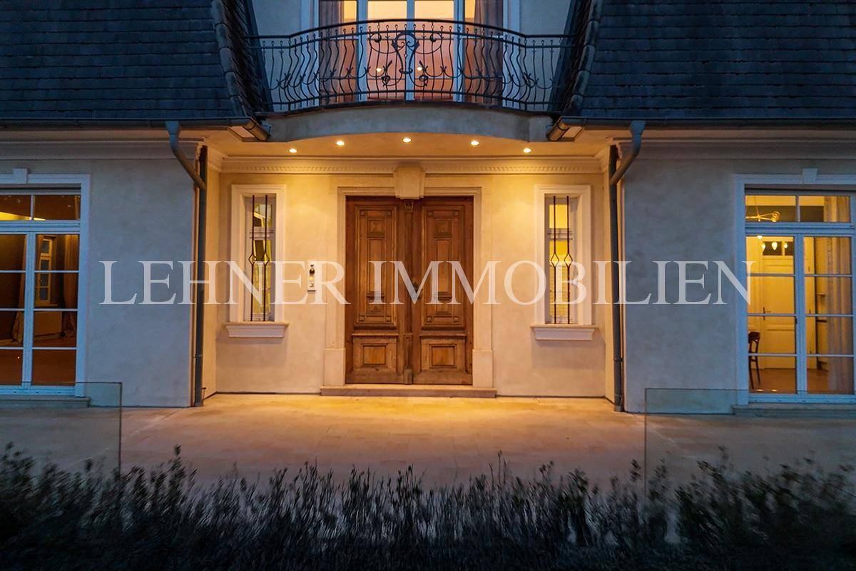 Beleuchteter Haupteingang der Villa mit Holztür und eleganten Laternen bei Nacht.