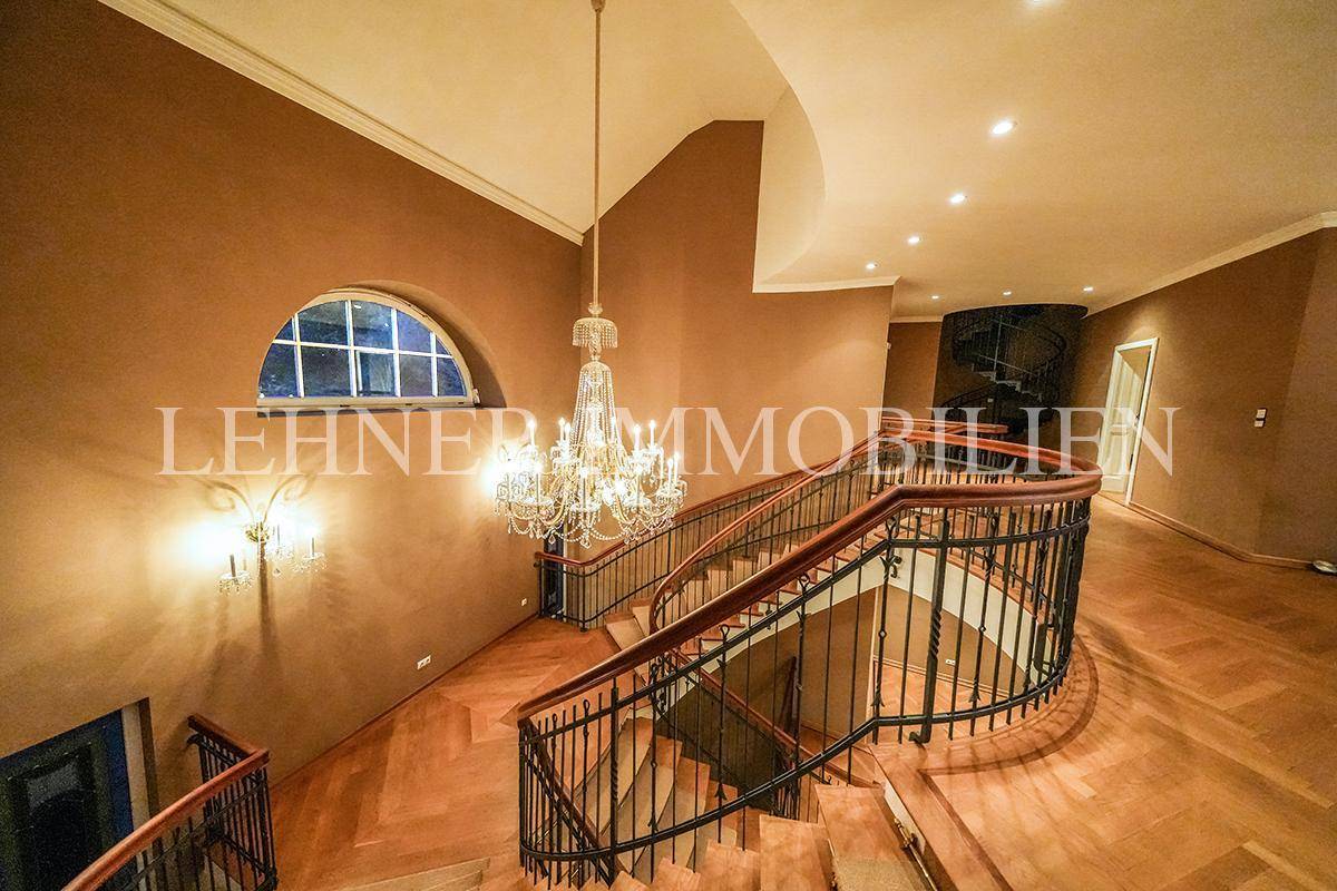 Geschwungenes Treppenhaus mit elegantem Kronleuchter, Buntglasfenster und Parkettboden.