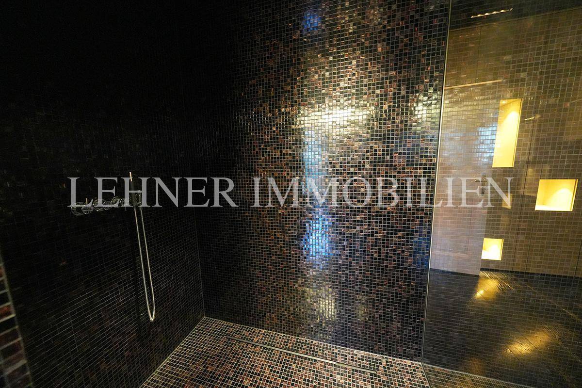 Moderne Duschkabine mit Mosaikfliesen und dunklem Design in einem luxuriösen Badezimmer.