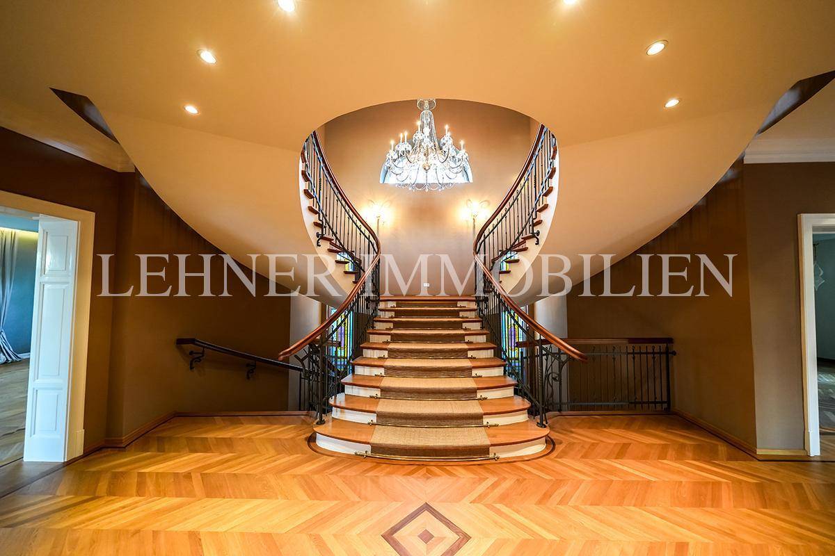 Prächtiges Treppenhaus mit geschwungener Doppeltreppe, Parkettboden und opulentem Kronleuchter.