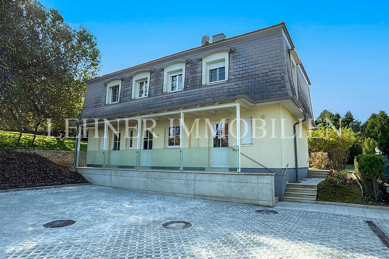 Seitenansicht der Villa mit überdachtem Eingangsbereich und gepflastertem Vorplatz.