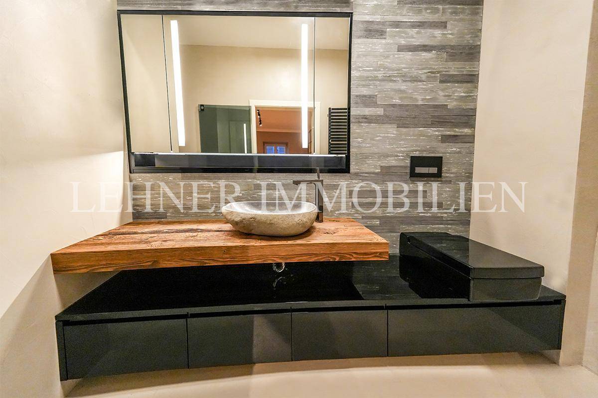Stilvolles Badezimmer mit Holzwaschtisch, Aufsatzwaschbecken und großem Spiegel mit Beleuchtung.