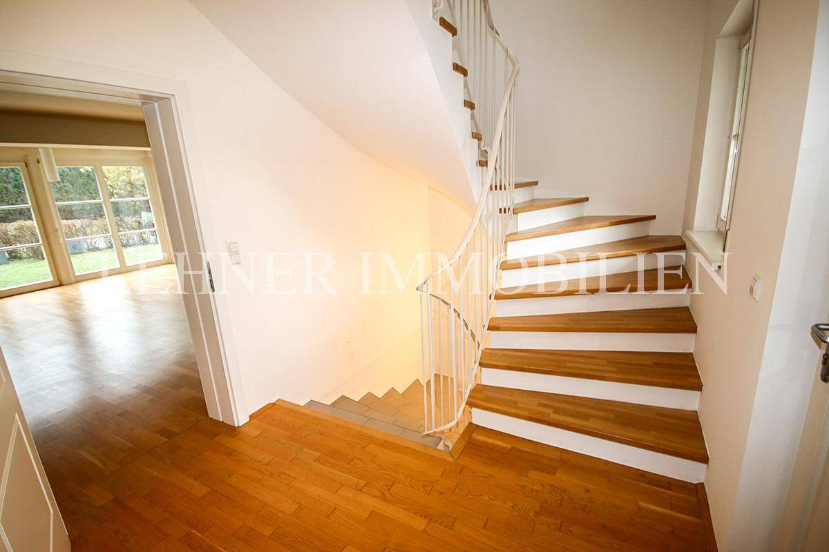 Heller Flur mit Holztreppe, Parkettboden und Blick in den angrenzenden Wohnbereich.