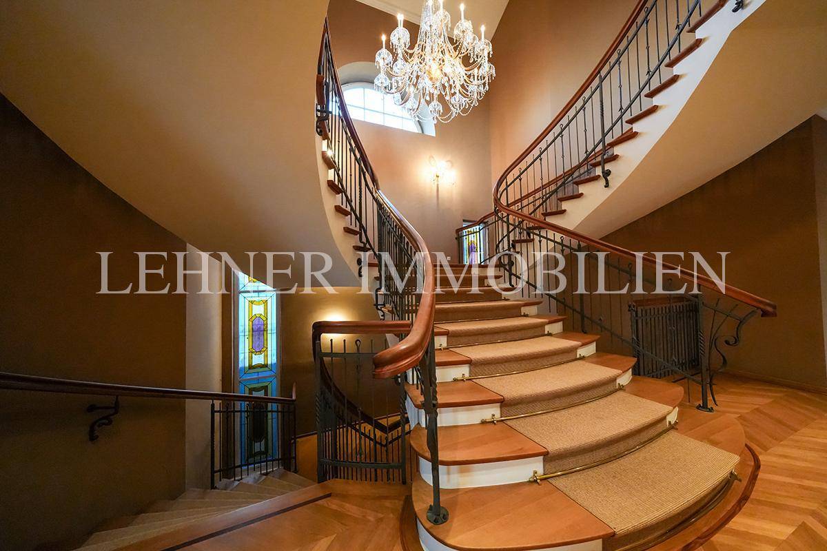 Geschwungenes Treppenhaus mit Holzgeländer, Teppichstufen und Blick auf ein Buntglasfenster.