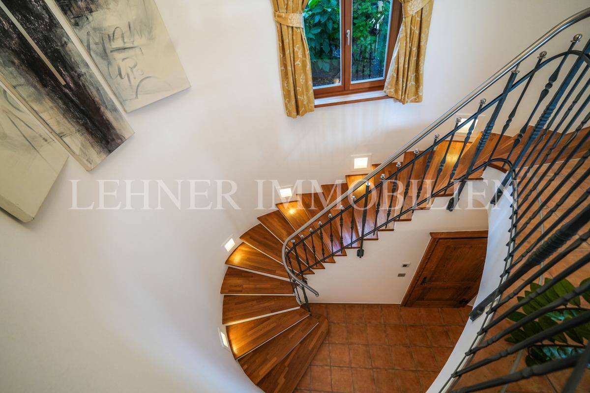 Blick von oben auf die geschwungene Holztreppe mit schmiedeeisernem Geländer.