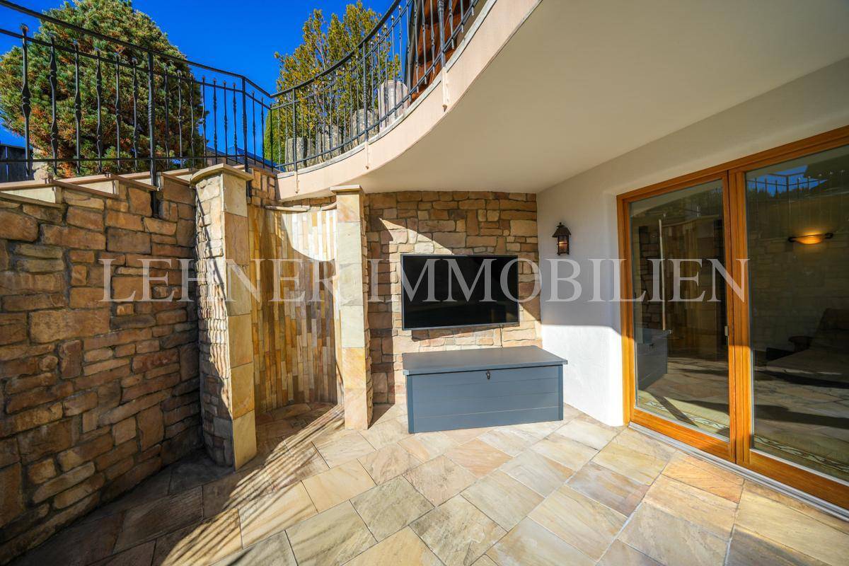 Terrassenbereich mit Natursteinwand, integriertem Fernseher und Zugang zum Innenbereich.