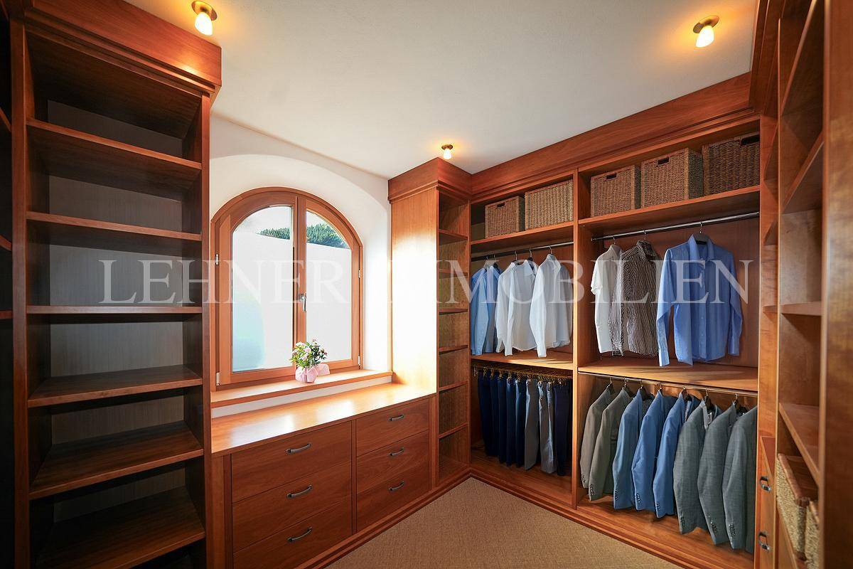 Geräumiger begehbarer Kleiderschrank mit Holzregalen, Schubladen und Fenster.