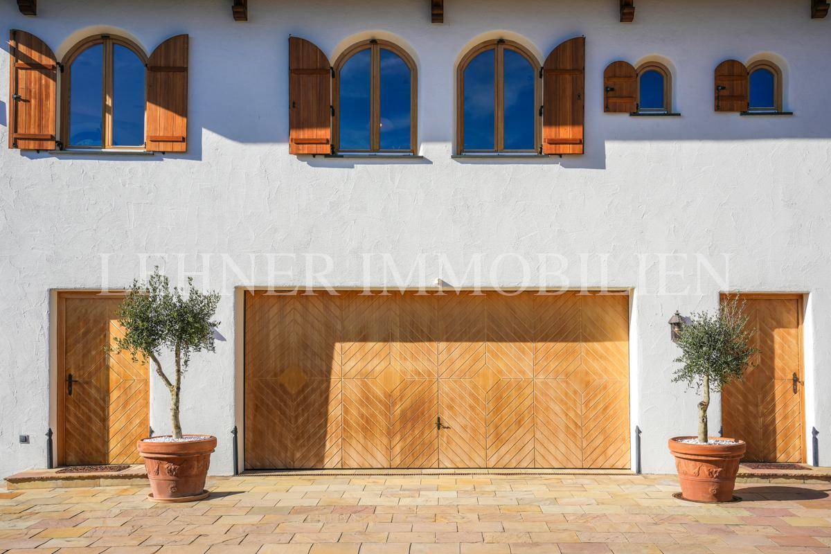 Garagentor und Seitentüren aus Holz mit dekorativen Topfbäumen und Außenleuchten.