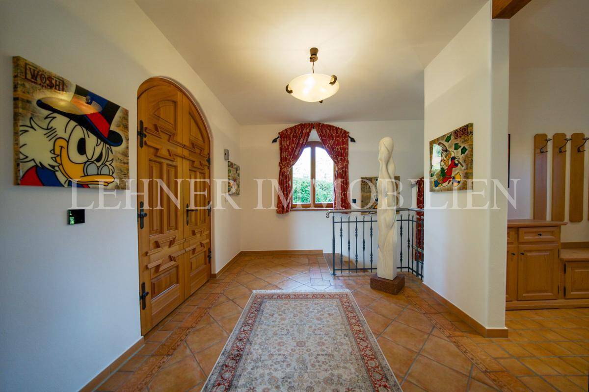 Eingangsbereich mit Terrakottafliesen, Holztür und Treppenaufgang.