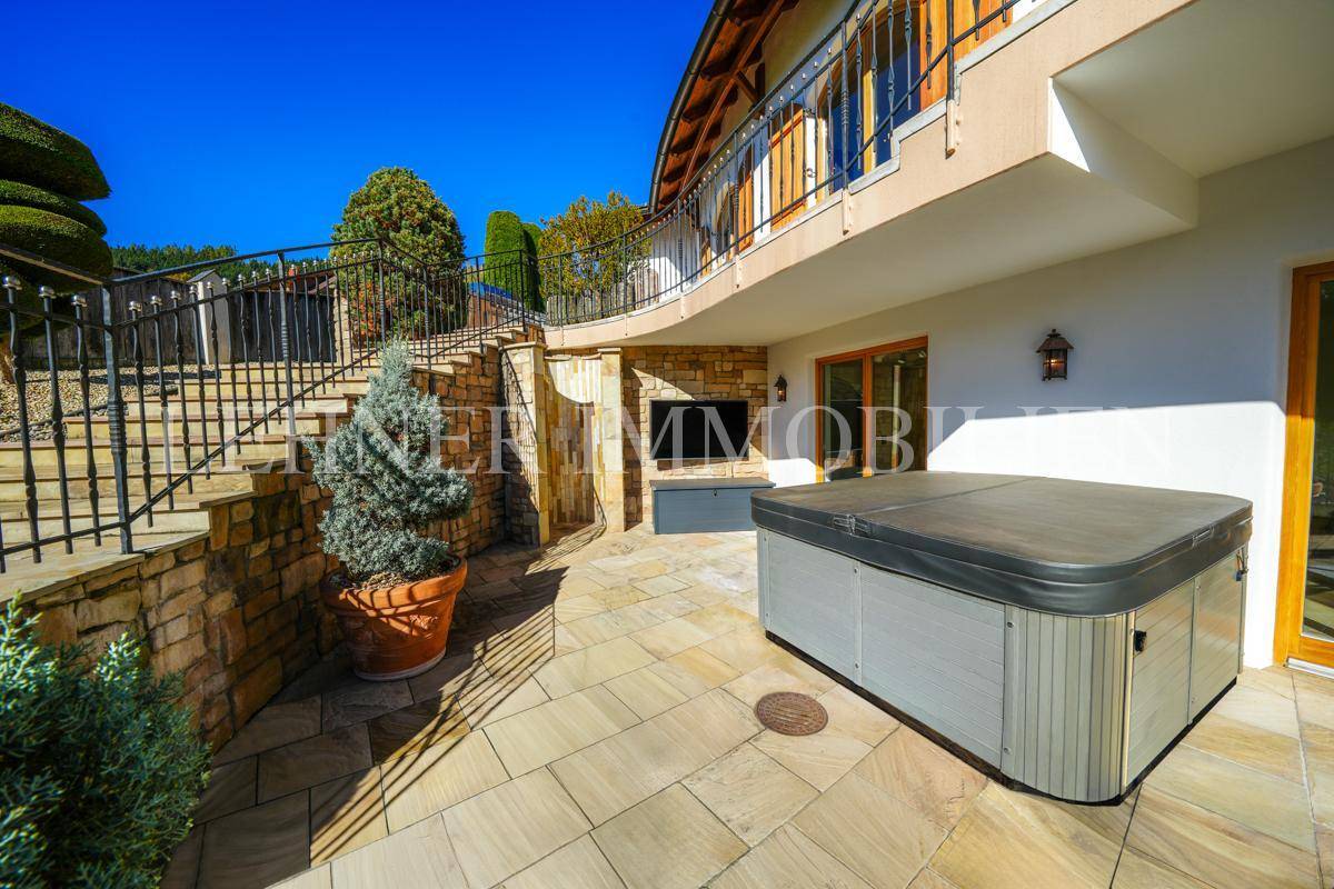 Terrassenbereich mit Whirlpool, Steintreppe und schmiedeeisernem Geländer in sonniger Umgebung.