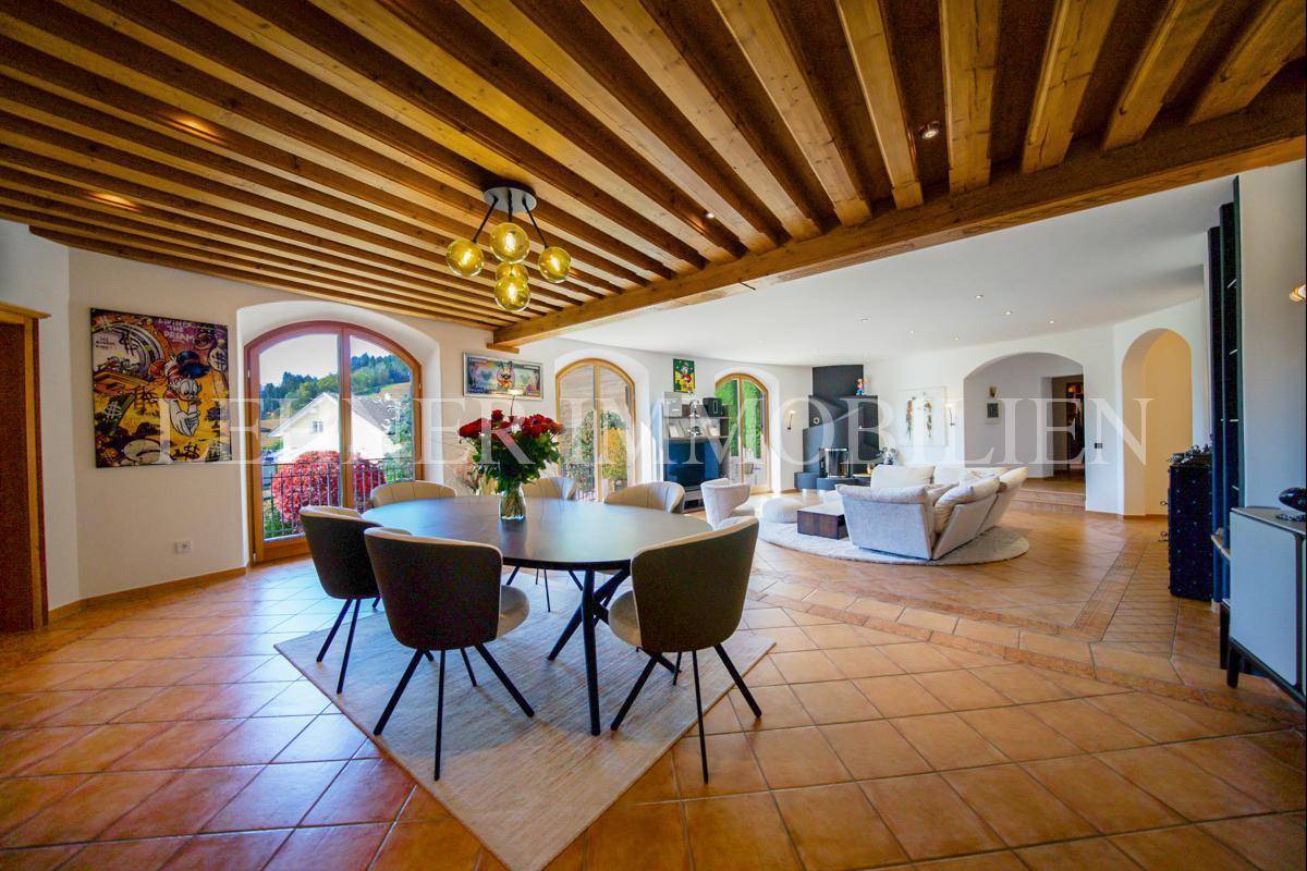 Offener Wohn- und Essbereich mit Holzbalkendecke, Terrakottafliesen und Blick ins Grüne.