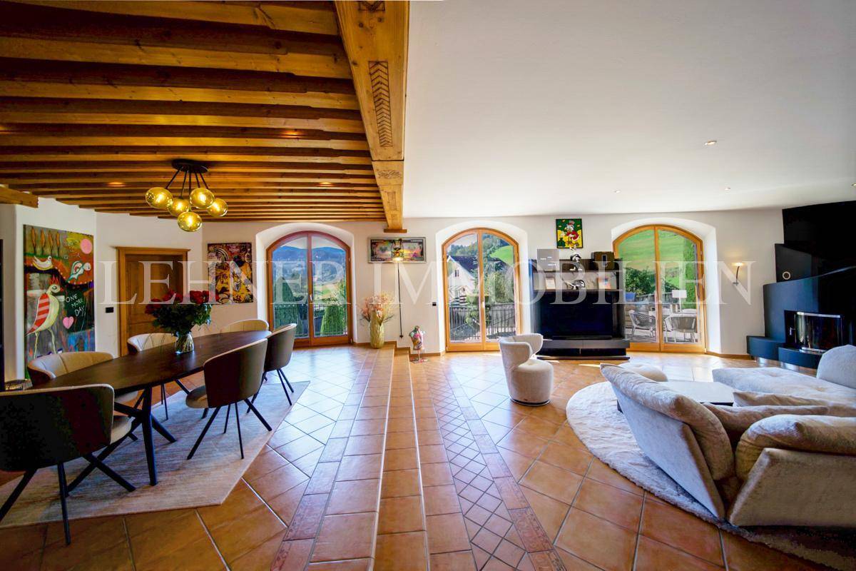 Geräumiger Wohn- und Essbereich mit Terrakottafliesen, Holzbalkendecke und Zugang zur Terrasse.
