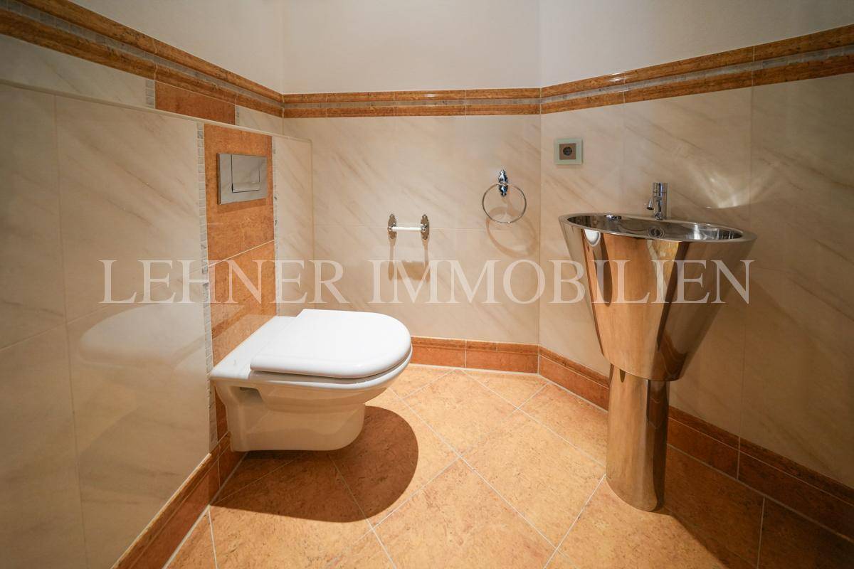 Badezimmer mit Wand-WC, modernem Waschbecken und Fliesen in Erdtönen.