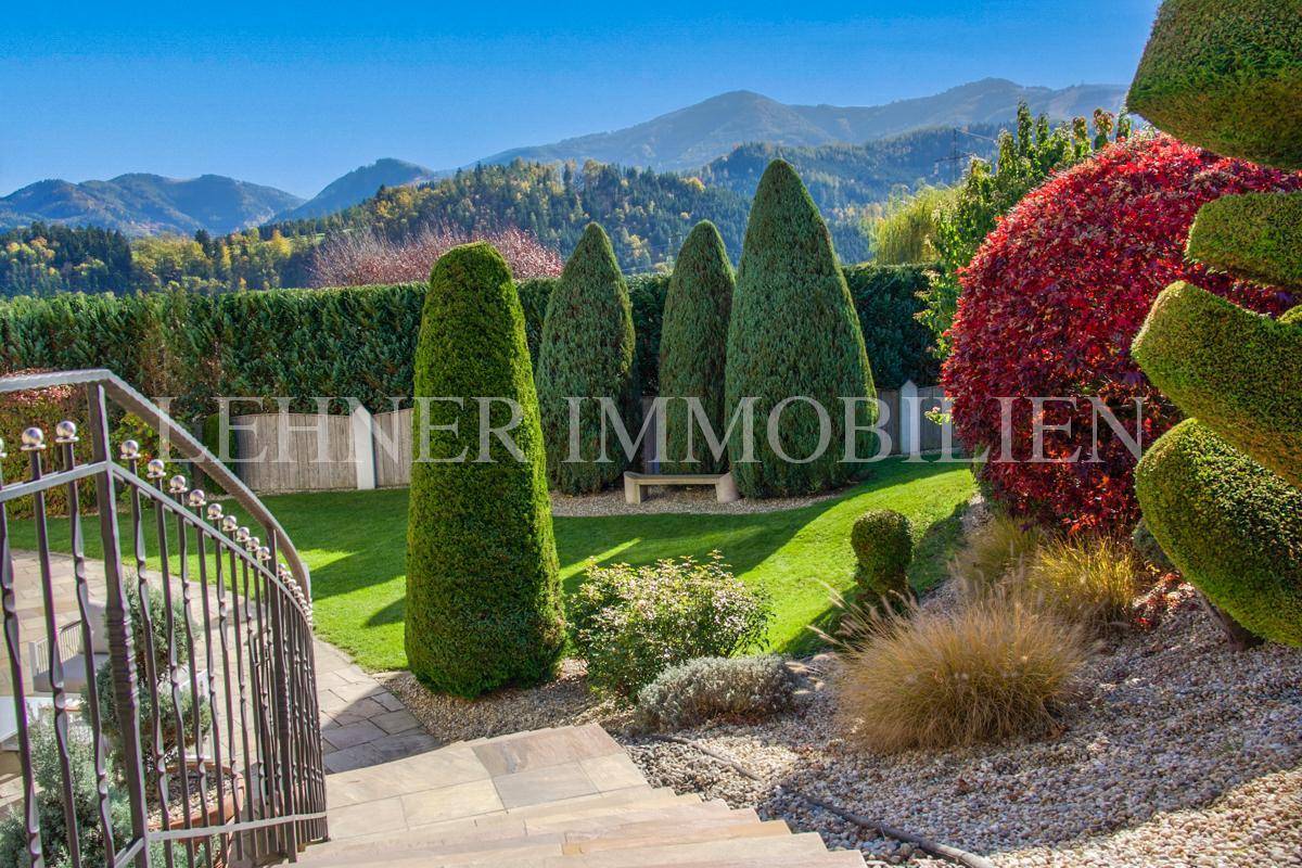 Gepflegter Garten mit Zierpflanzen, Steintreppen und weitem Blick auf die Berge.