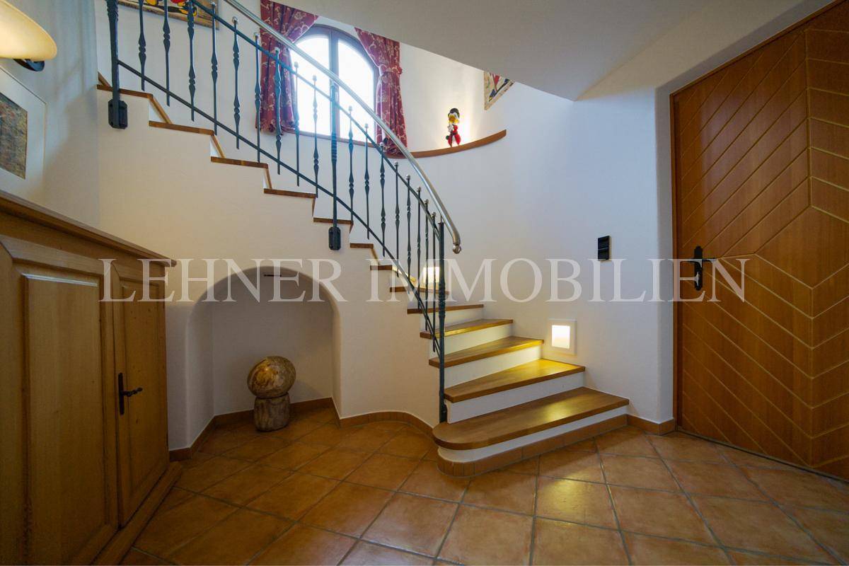 Geschwungene Holztreppe mit schmiedeeisernem Geländer und Terrakottafliesen im Eingangsbereich.