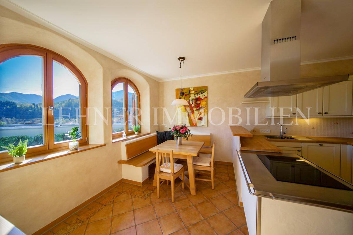 Helle Einbauküche mit Essbereich, Terrakottafliesen und großen Fenstern mit Bergblick.