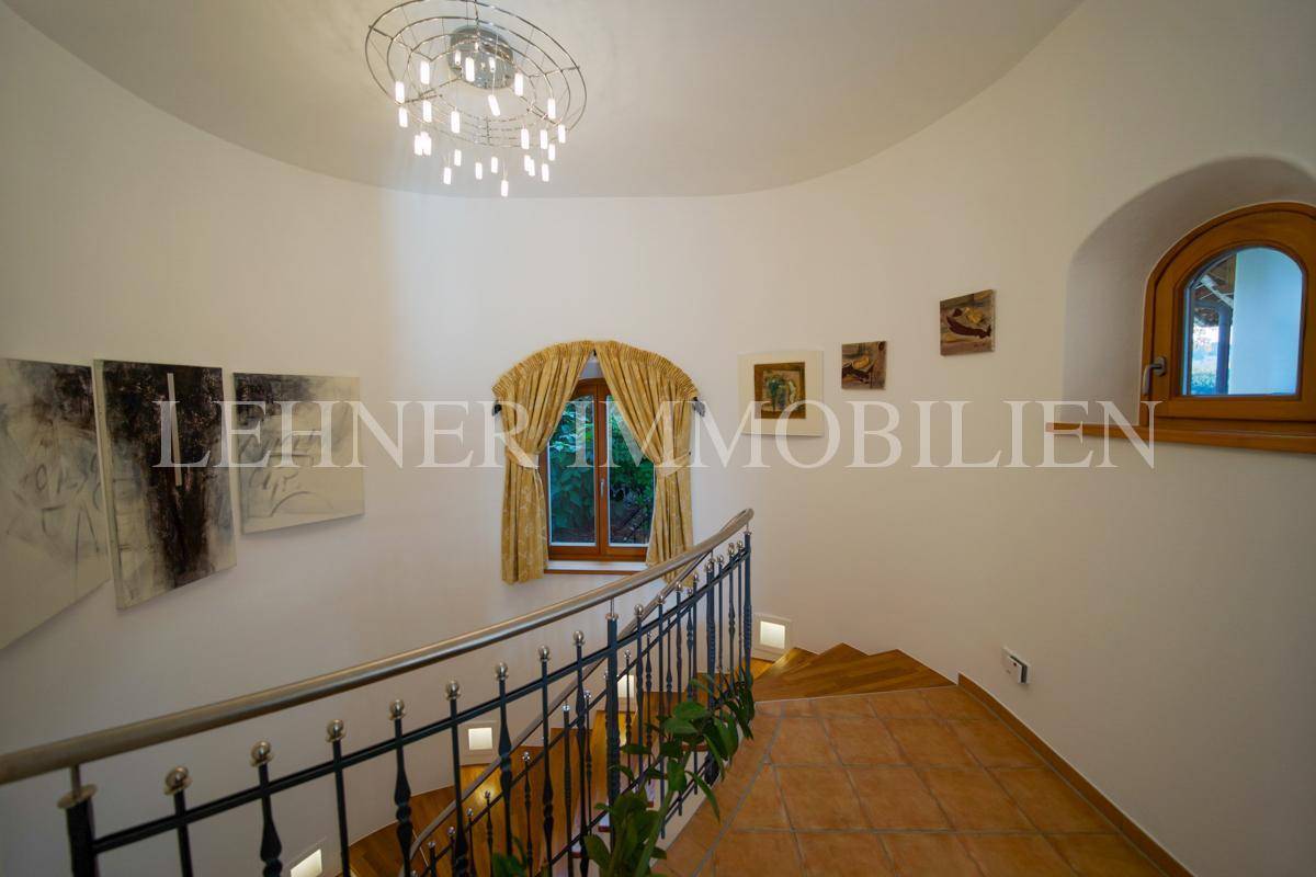 Geschwungener Treppenaufgang mit schmiedeeisernem Geländer und runden Fenstern.