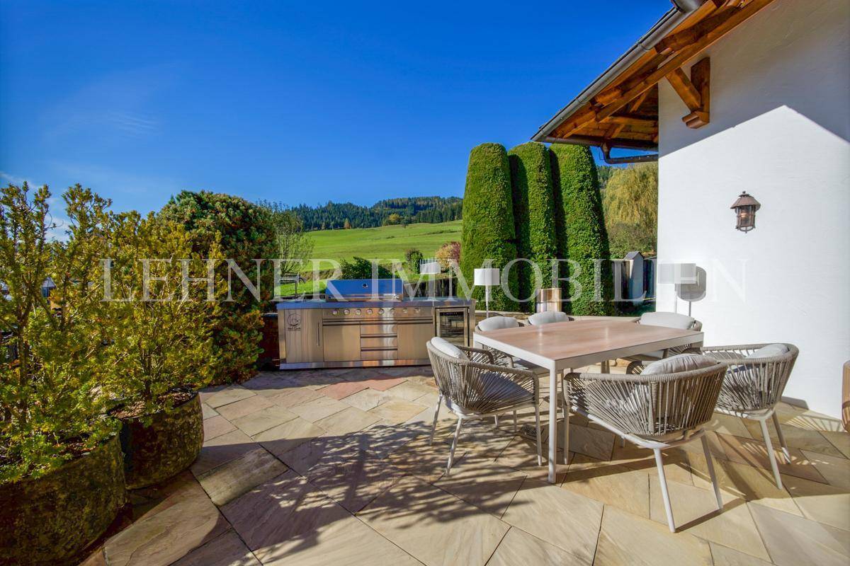 Sonniger Terrassenbereich mit Esstisch, Außenküche und Blick auf die grüne Landschaft.