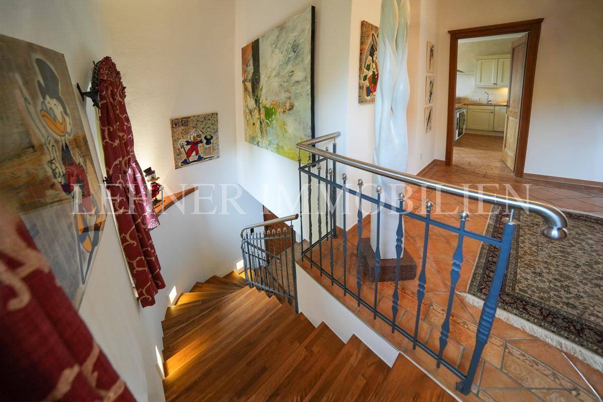 Treppenhaus mit Holzstufen, schmiedeeisernem Geländer und Terrakottafliesen.