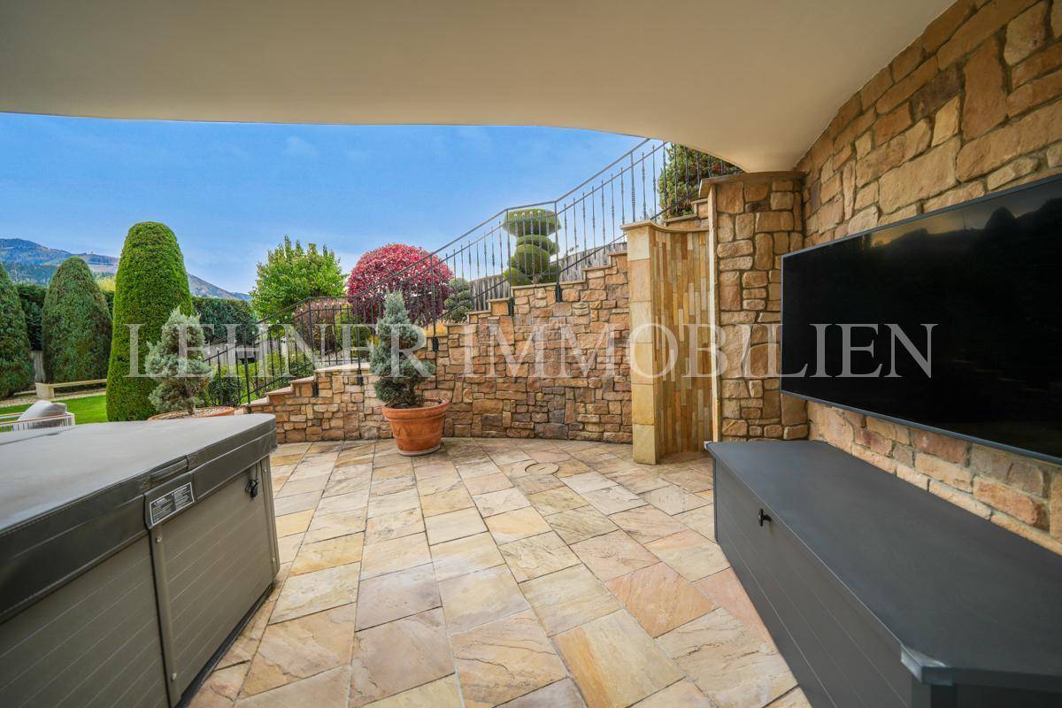 Überdachter Terrassenbereich mit Natursteinwand, integriertem Fernseher und Whirlpool.