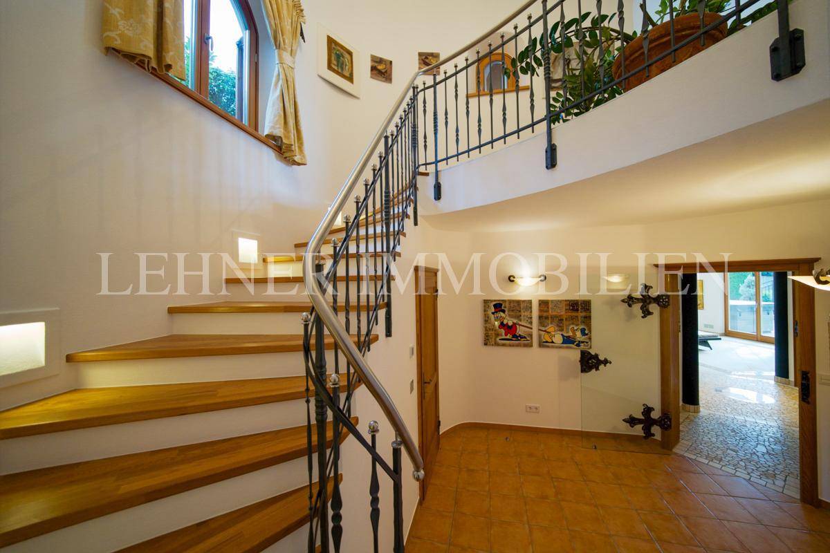 Treppenhaus mit Holzstufen, schmiedeeisernem Geländer und Terrakottafliesen.