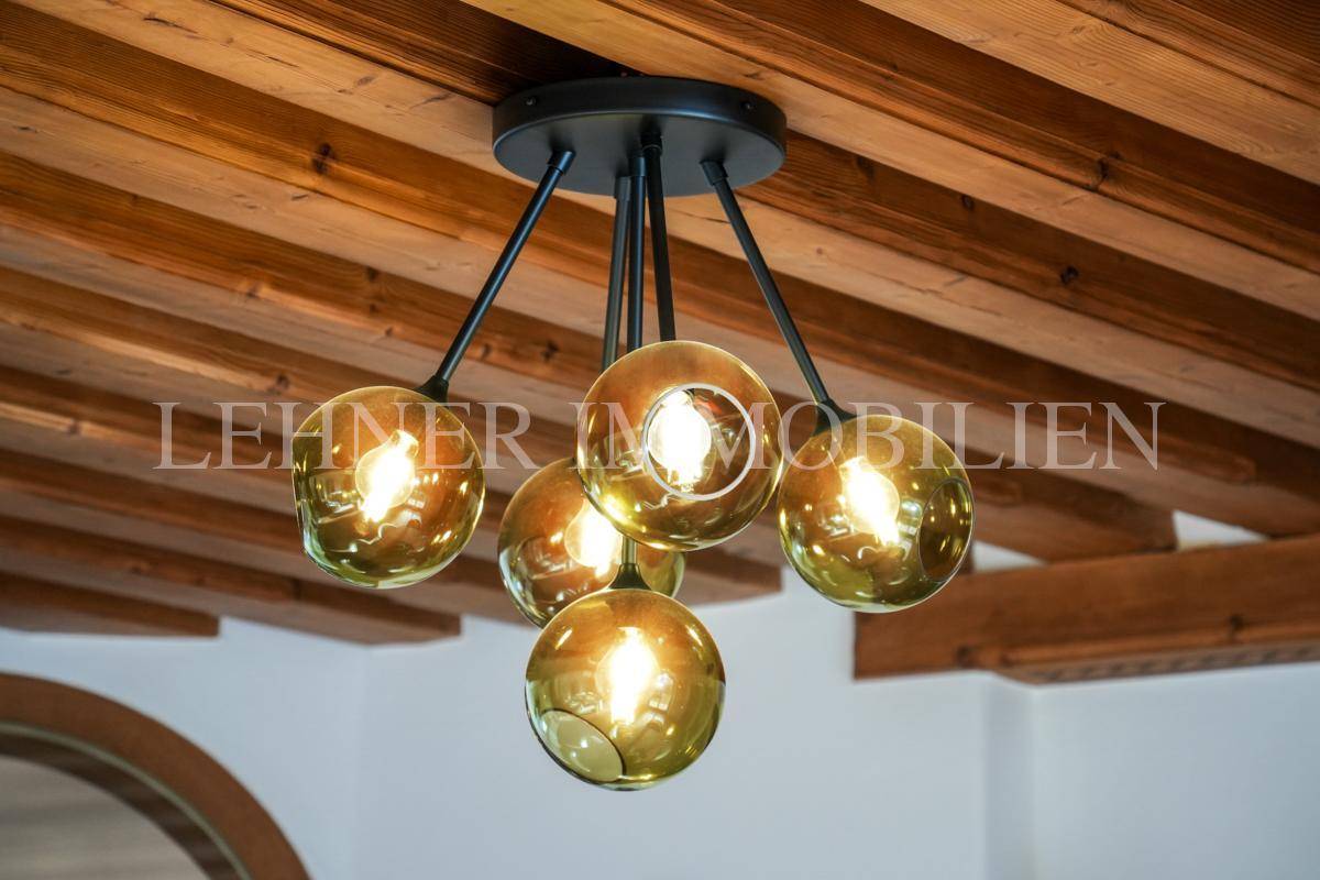 Detailaufnahme eines modernen Kronleuchters mit fünf kugelförmigen Leuchten an der Holzbalkendecke.