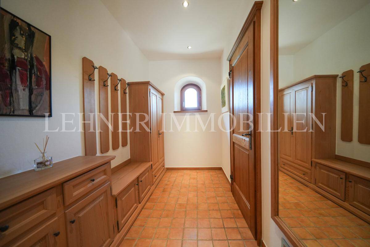 Flur mit Holzmöbeln, Garderobe und Terrakottafliesen, mit kleinem Fenster.