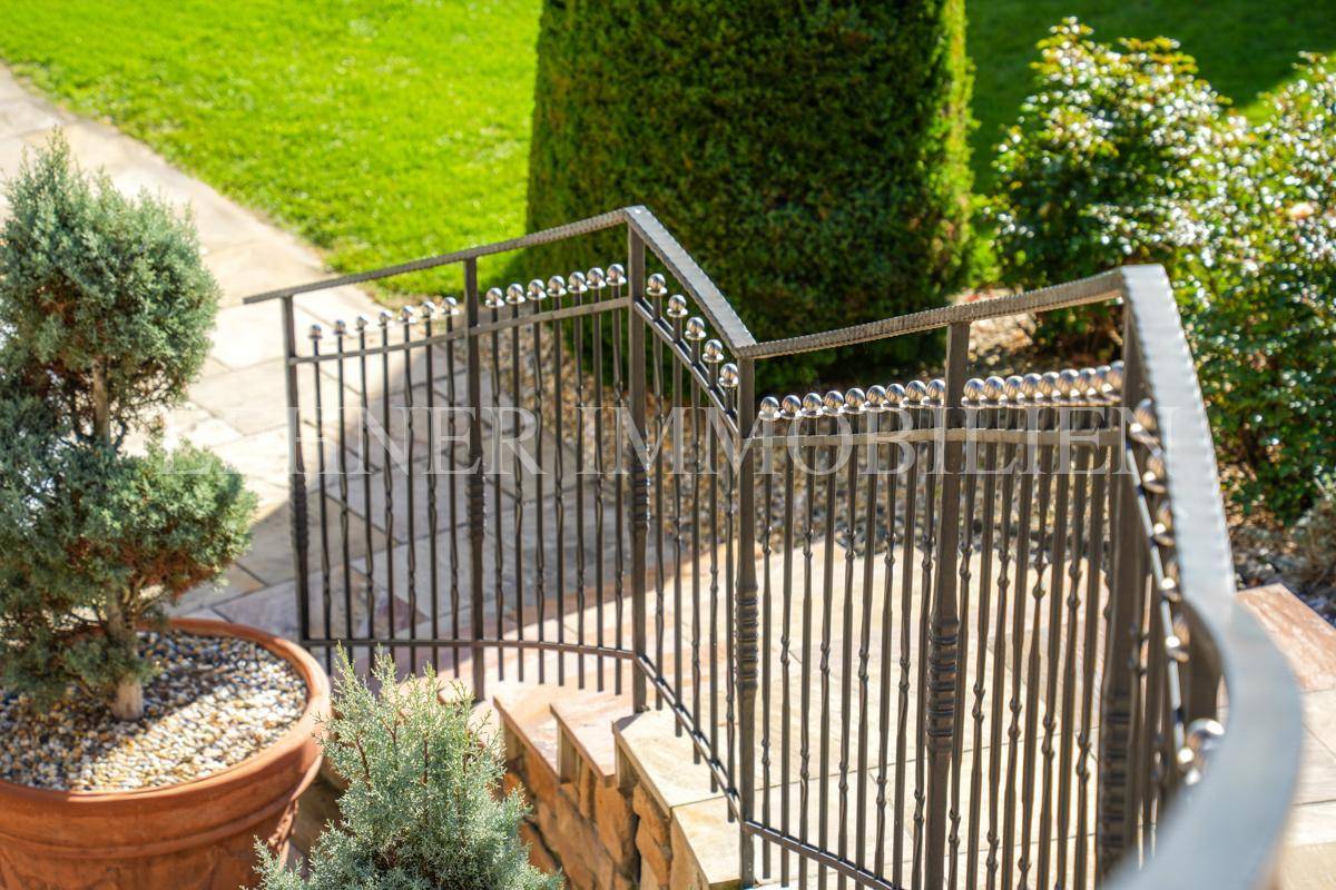 Detailansicht des schmiedeeisernen Geländers einer Steintreppe im gepflegten Garten.