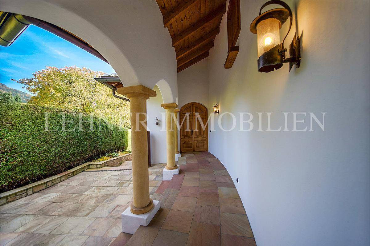 Überdachter Eingangsbereich mit Säulen, Holztür und schmiedeeisernen Laternen.